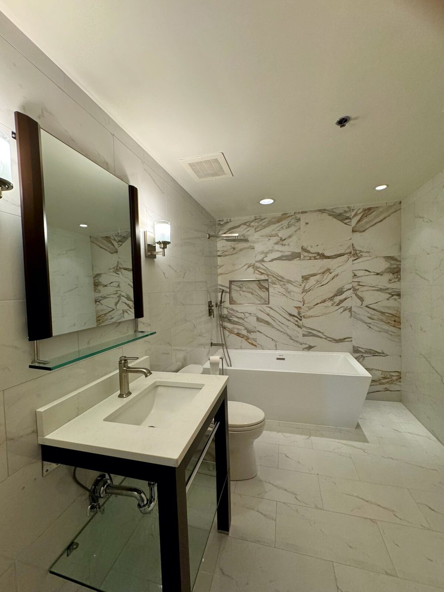 Bathroom after renovation, with white veined wall tile, a rectangular freestanding tub and an open shower area
